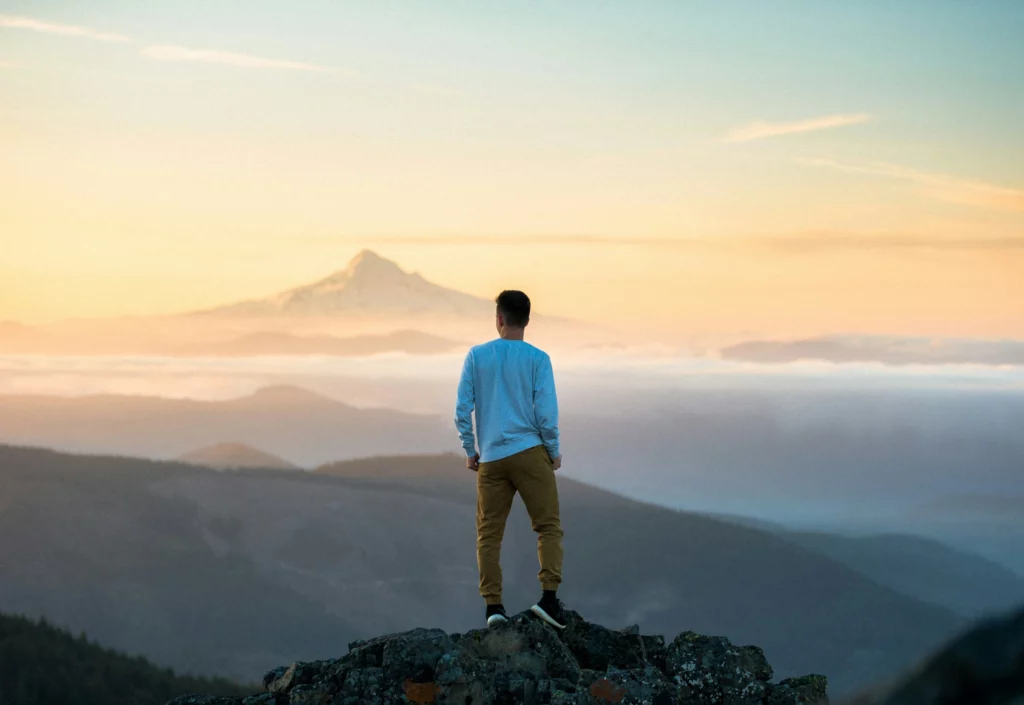 Un homme se tient debout sur une colline il regarde le lever de soleil sur une chaîne de montagnes. Cette image illustre la page "Qui suis-je ?"